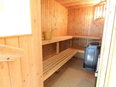 An interior of a wooden sauna with benches a bucket and a heater at The Hayloft in St Florence