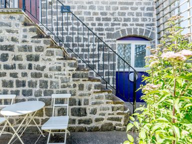 An outdoor stone staircase with a black railing next to a round white table and two white chairs with plants nearby at The Hayloft in St Florence