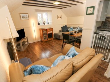 A living room with a beige sofa blue cushions wooden floor dining table and chairs next to a kitchen with a washing machine at The Hayloft in St Florence
