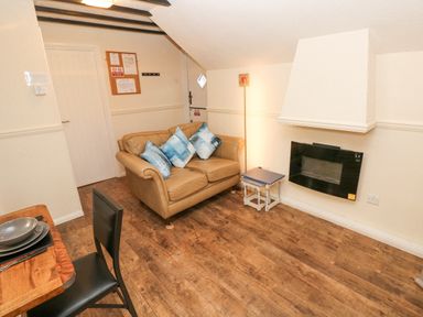 A small living room with a leather sofa blue cushions wall mounted fireplace wooden floor and dining table with chairs at The Hayloft in St Florence