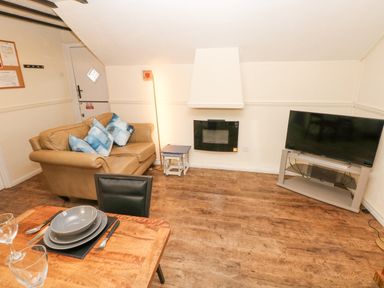 A living room with a brown sofa and blue pillows a television on a stand and a wooden dining table at The Hayloft in St Florence
