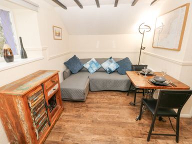 A small living room with a sectional sofa and square wooden dining table with two chairs at The Hayloft in St Florence