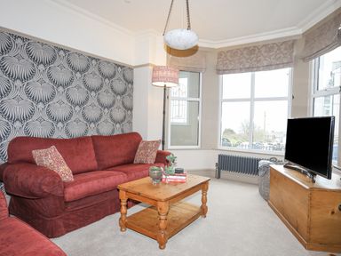 A living room with a red sofa a wooden coffee table a television on a wooden stand and patterned wallpaper at Llwyn Onn in Criccieth