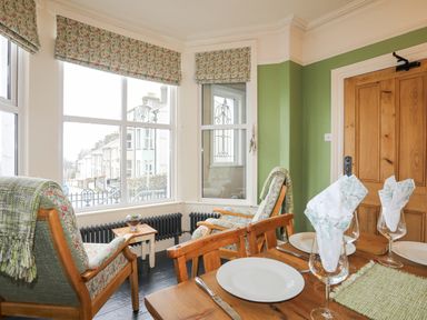 A dining area with set table and two armchairs by windows in a room with green walls at Llwyn Onn in Criccieth