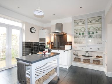 A kitchen with an island table and glass front cabinet at Llwyn Onn in Criccieth