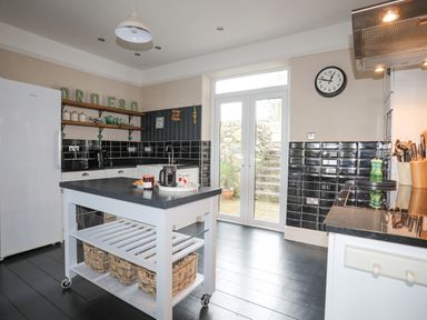 A kitchen with a white island cart with baskets below and black countertops at Llwyn Onn in Criccieth