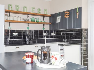 A kitchen with black tiled backsplash white cabinets a coffee press and mug on a counter at Llwyn Onn in Criccieth