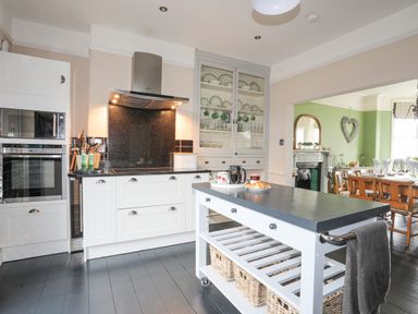 A kitchen with a cooking island and built in oven next to a dining room with a table at Llwyn Onn in Criccieth