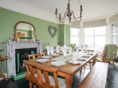 A dining room with a wooden table set with plates and glasses by windows at Llwyn Onn in Criccieth