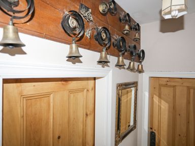 A hallway with wooden doors a mirror on the wall and a row of brass bells mounted on a wooden board at Llwyn Onn in Criccieth