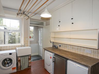 A utility room with washing machine dryer sink and storage cabinets at Llwyn Onn in Criccieth
