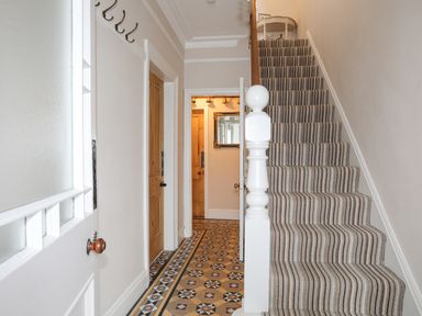 A hallway with patterned tile floor and striped carpeted stairs at Llwyn Onn in Criccieth