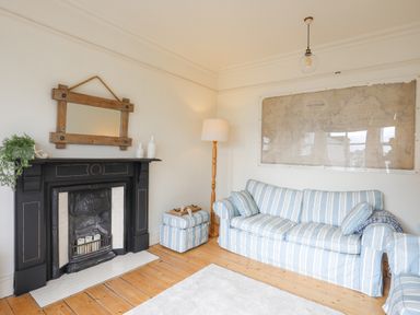 A living room with striped sofa ottoman floor lamp and a fireplace at Llwyn Onn in Criccieth