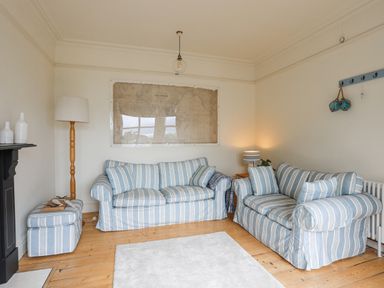 A living room with two striped sofas a floor lamp a table lamp and a large wall map at Llwyn Onn in Criccieth