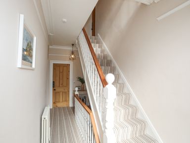 A hallway with striped carpeted stairs a wooden door a small table with a plant and a chandelier at Llwyn Onn in Criccieth