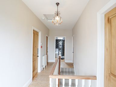 A hallway with wooden doors and a staircase with a striped carpet at Llwyn Onn in Criccieth