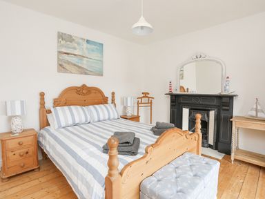 A bedroom with a wooden bed with striped bedding two bedside tables lamps a fireplace and a cushioned bench at Llwyn Onn in Criccieth