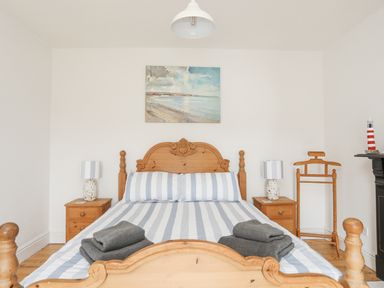 A bedroom with a wooden bed with striped bedding two bedside tables with lamps and a wooden valet stand at Llwyn Onn in Criccieth