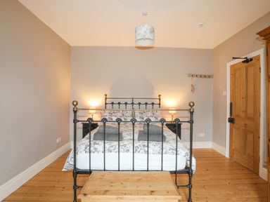 A bedroom with a metal bed frame two nightstands with lamps folded towels on the bed a wooden floor and a wooden door at Llwyn Onn in Criccieth