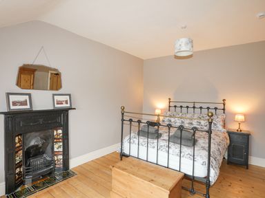 A bedroom with a metal bed wooden chest bedside tables with lamps and a fireplace at Llwyn Onn in Criccieth