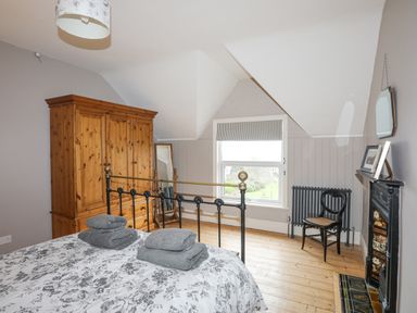 A bedroom with a bed folded towels wardrobe mirror window chair radiator and fireplace at Llwyn Onn in Criccieth