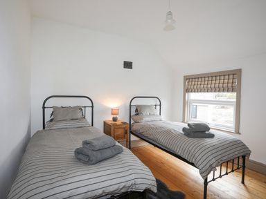 A bedroom with two single beds with striped bedding and folded towels on each bed at Llwyn Onn in Criccieth