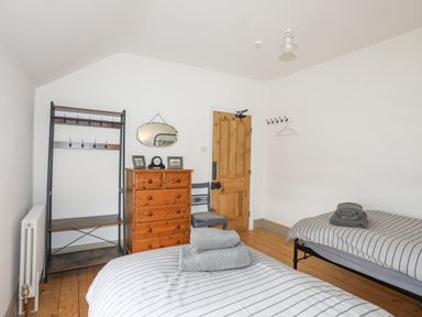 A bedroom with two single beds a wooden chest of drawers a chair a coat rack and a wall mirror at Llwyn Onn in Criccieth