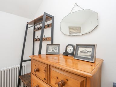 A wooden dresser with two framed pictures and a clock on top with a mirror hanging above and a coat rack next to it at Llwyn Onn in Criccieth