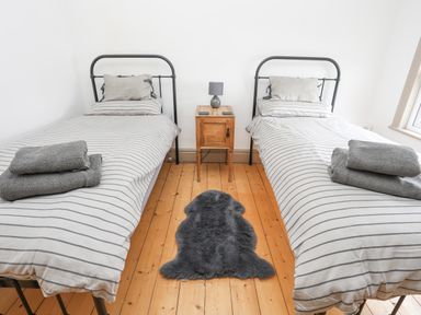 A bedroom with two single beds with striped bedding a wooden nightstand with a lamp and a dark rug on a wooden floor at Llwyn Onn in Criccieth