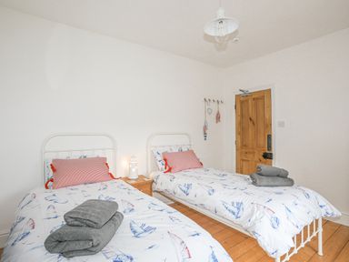 A bedroom with two single beds with boat patterned bedding and pink pillows at Llwyn Onn in Criccieth