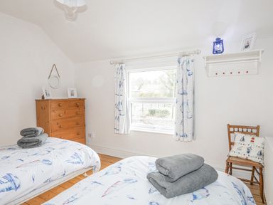 A bedroom with two single beds with folded towels a wooden chest of drawers a wooden chair and a window with curtains at Llwyn Onn in Criccieth