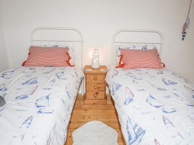 A bedroom with two single beds with sailboat patterned bedding and a wooden nightstand with a lighthouse lamp between beds at Llwyn Onn in Criccieth