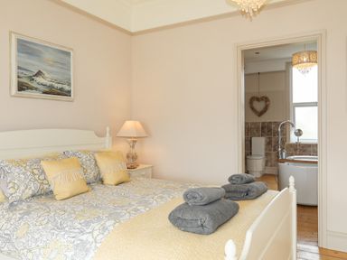 A bedroom with a bed with yellow and gray bedding and folded towels leading to a bathroom at Llwyn Onn in Criccieth