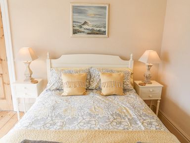 A bedroom with a double bed two bedside tables with lamps and a painting above the bed at Llwyn Onn in Criccieth