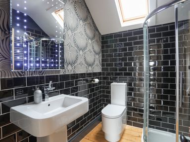A bathroom with a sink toilet and shower with black tiles and patterned wallpaper at Llwyn Onn in Criccieth