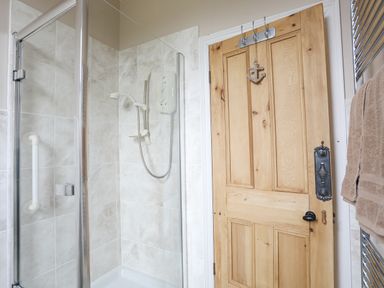 A shower area with tiled walls and a wooden door with hooks and a towel on a rack at Llwyn Onn in Criccieth