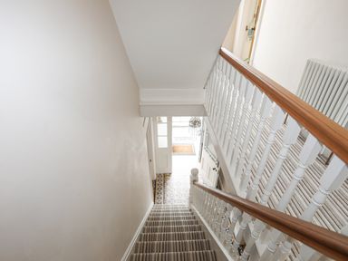 A staircase with striped carpet and white wooden banister overlooking a tiled entrance hall at Llwyn Onn in Criccieth
