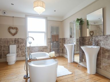 A bathroom with a bathtub toilet two sinks a window and a wooden floor at Llwyn Onn in Criccieth