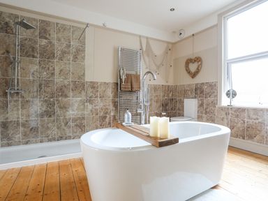 A bathroom with a freestanding bathtub with candles a walk-in shower a toilet and a window at Llwyn Onn in Criccieth