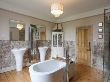 A bathroom with a freestanding bathtub two pedestal sinks a wooden door and a cabinet at Llwyn Onn in Criccieth