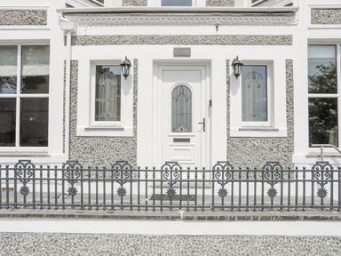 A front entrance door with glass panels flanked by two windows and black metal fence at Llwyn Onn in Criccieth