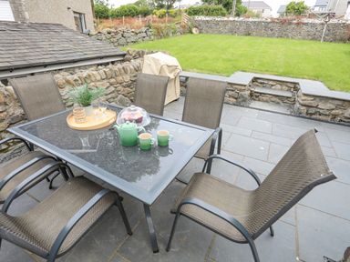 An outdoor patio with a glass table and four chairs near a grassy yard at Llwyn Onn in Criccieth