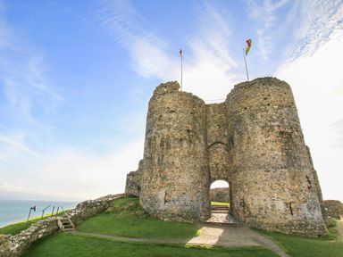 An ancient stone castle with two round towers and flags on top by the sea at Llwyn Onn in Criccieth