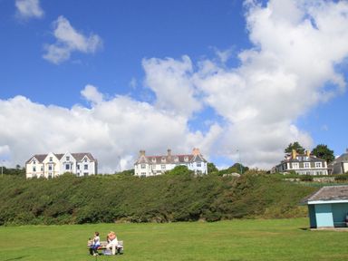 A large green field with two people sitting on a bench and houses on a hill in the background at Llwyn Onn in Criccieth