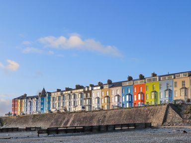 A row of colorful multi-story houses along a stone seawall overlooking a beach at Llwyn Onn in Criccieth