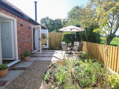 A garden patio with outdoor table and chairs under an umbrella next to a brick house at Beck View in Weston Longville near Lenwade