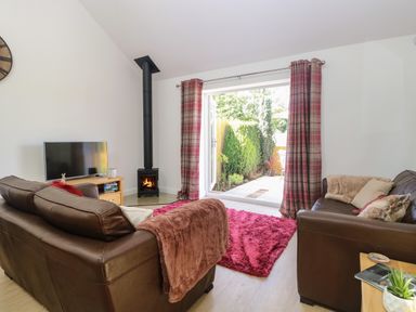 A living room with two brown sofas a fireplace and open doors to a garden at Beck View Weston Longville near Lenwade