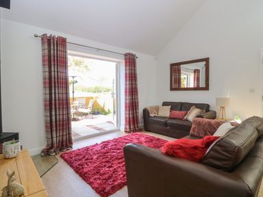A living room with brown leather sofas and red rug near patio doors at Beck View Weston Longville near Lenwade