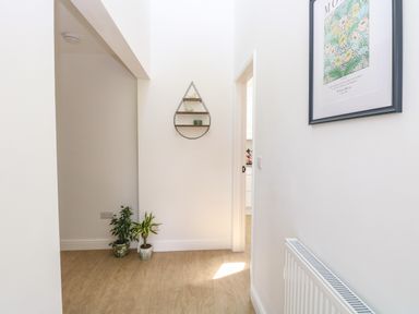 A hallway with two potted plants on the floor a wall shelf and a framed picture on the wall at Beck View in Weston Longville near Lenwade