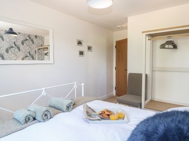 A bedroom with a bed with rolled towels and a tray with drinks and pastries a chair and an open wardrobe at Beck View in Weston Longville near Lenwade
